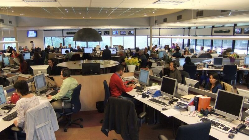 Editors at work around the central desk of a modern newsroom